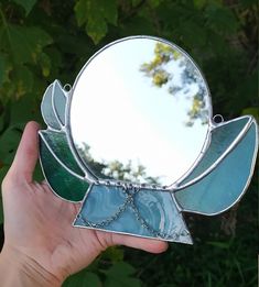 a hand holding up a small mirror with leaves on it