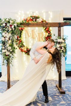 a bride and groom kissing in front of an arch decorated with flowers