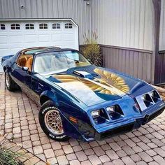 a blue pontiac firebird parked in front of a garage