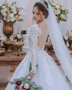 a woman wearing a wedding dress and holding a bouquet in front of a table with flowers