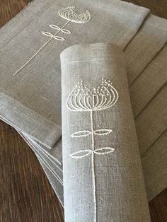 four linen napkins with embroidered designs on them sitting on top of a wooden table