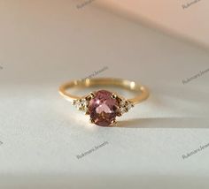 a ring with an oval shaped pink stone surrounded by small white diamonds on a table