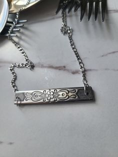 a silver necklace sitting on top of a table next to a fork and spoons