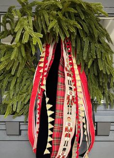 a christmas wreath with ribbons hanging from it's front door, decorated with evergreen branches