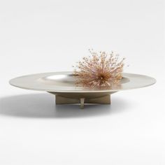 a white plate topped with a pink flower on top of a metal stand in front of a white wall