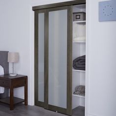 a white closet with glass doors and clothes hanging on the wall next to a night stand