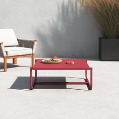 a red coffee table sitting on top of a cement floor next to a white chair