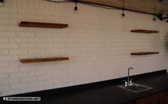 a white brick wall with wooden shelves on the side and a black counter in front