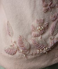 a pink sweater with beaded flowers on the chest and sleeves is seen in this close up photo