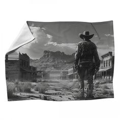 a black and white photo of a cowboy standing in front of an old western town