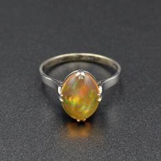 "A rainbow is swimming in this gorgeous antique opal ring! A beautifully proportioned opal cabochon is centered with cardinal prongs (north, south, west and east) in an 18k white gold setting. The opal features a transparent orange body, typical of Mexican jelly opals, with a \"contra luz\" color flash seen when the gem interacts with light. The color play is astounding, with every color of the rainbow ignited within the body of the opal, having painterly brush-stroke like patterns. This ring hails from the 1920s and has been tenderly well-cared for in its lifetime. It is in wonderful condition and ready for a new owner. This ring could be a perfect alternative engagement ring, gift for someone with an October birthstone or simply a present for an antique jewelry lover.   Opal is a fascina Classic Opal Moonstone Ring As Gift, Vintage Opal Ring As A Gift, Oval Cabochon Opal Ring With Polished Finish, Vintage Opal Ring With Polished Finish For Formal Occasions, Classic Oval Opal Ring With Polished Finish, Fine Jewelry Oval Cabochon Opal Ring, Ethiopian Opal Oval Rings For Anniversary, Oval Cabochon Opal Ring Fine Jewelry, Oval Cabochon Opal Ring In Fine Jewelry