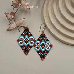 a pair of beaded earrings sitting on top of a white plate next to a plant