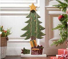 a wooden christmas tree with presents under it on the floor next to a basket full of gifts