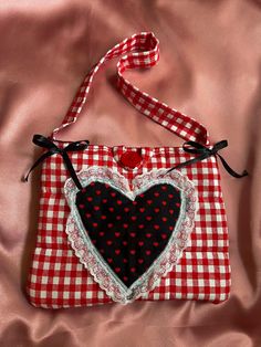 a red and white checkered bag with a black heart on the front, sitting on a pink satin surface