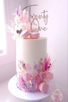 a white cake with pink frosting and flowers on top, next to a sign that says twenty one