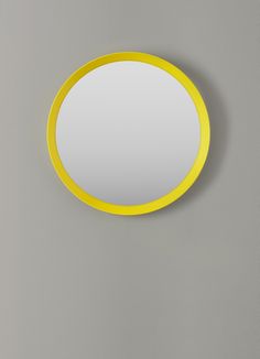 a round mirror hanging on the wall in a room with grey walls and yellow trim