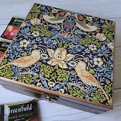 an ornate box with birds and flowers painted on the lid sits next to some tea bags