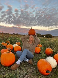 a woman is sitting in a field with pumpkins on her head and arms behind her head