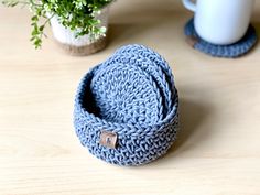 a crocheted blue ring sits on a table next to a coffee cup and plant