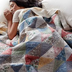 a woman laying in bed under a blanket with her hand on her chin and looking at the camera