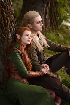 two people sitting next to each other in front of a tree and one person with long red hair