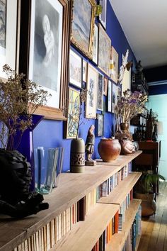 a long shelf with vases and pictures on it next to a wall full of books