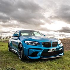 a blue bmw car parked on top of a lush green field under a cloudy sky