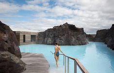 a woman is walking up the stairs into a blue pool with rocks on both sides