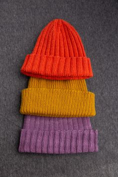 three knitted beanies sitting on top of each other, one orange and one purple