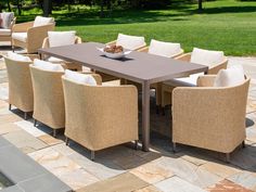 an outdoor dining table and chairs set up on a stone patio with grass in the background