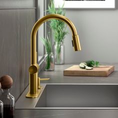 a gold faucet on a kitchen counter next to a cutting board with cucumbers