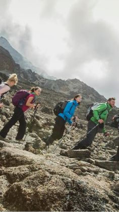 a group of people hiking up the side of a rocky mountain with mountains in the background