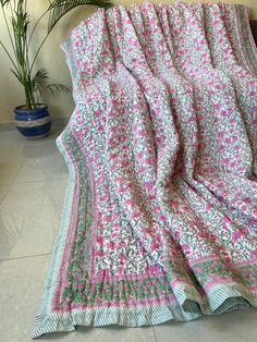 a pink and green blanket sitting on top of a floor next to a potted plant