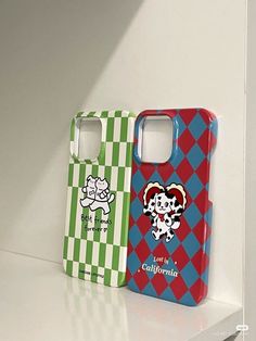 two cell phones are sitting next to each other on a white shelf with green, red and blue checkered covers