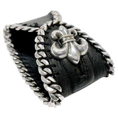 Fleur De Lis Leather Bracelet by Chrome Hearts. This distinctive bracelet features a unique blend of materials with a 925 silver curbed chain sewn into black leather, highlighted by a Silver Fleur de Lis charm serving as the toggle closure. The combination of silver and leather gives it a rugged yet elegant look. The charm/toggle is stamped with the CH (Chrome Hearts hallmark), 925, and the year 2005. The bracelet measures 2.25" in width and 7" in length, weighing 72.2 grams. Formal Engraved Leather Jewelry, Luxury Leather Bracelet Engraved, Silver Leather Bracelets For Formal Occasions, Elegant Engraved Leather Jewelry, Designer Leather Jewelry For Gift, Designer Leather Jewelry As A Gift, Formal Silver Leather Bracelets, Black Leather Bracelets With Sterling Silver Clasp, Silver Leather Cuff Bracelet Gift