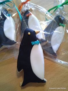 three penguin shaped cookies sitting on top of a wooden table next to plastic bags filled with frosting