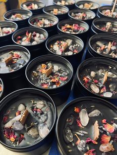 many black bowls filled with different types of rocks and flowers on top of a table