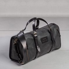 a black leather duffel bag sitting on top of a white floor next to a wall