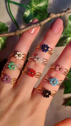 a woman's hand with five different colored rings on her fingers and one is holding a twig