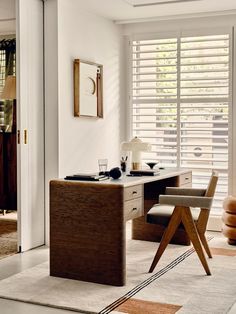 a room with a desk, chair and mirror that has shutters on the windows