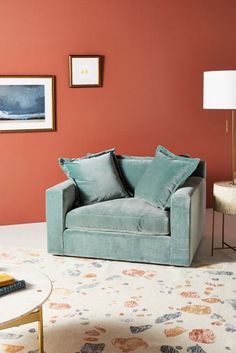 a living room with an orange wall and blue chair in the corner, next to a white coffee table