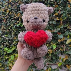 a hand holding a crocheted teddy bear with a red heart in its paws