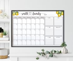 a family calendar hanging on the wall next to a potted plant in front of a fireplace