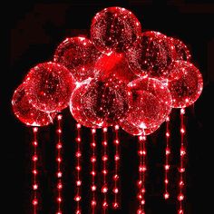 a bunch of red balloons that are hanging from strings on a pole in the dark