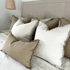 three pillows on top of a bed with white linens and brown trim around the edges