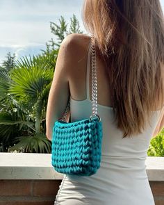 a woman holding a blue crocheted purse on top of her shoulder and looking at the sky