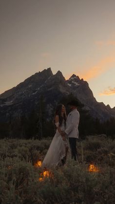 a bride and groom standing in front of the mountains at sunset