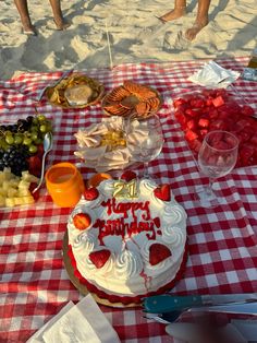 a birthday cake sitting on top of a red and white checkered table cloth covered in fruit