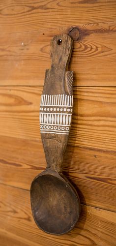 an old wooden spoon hanging on the wall next to a wood paneled wall with a fish design