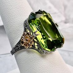 I now offer this lovely filigree reproduction in sterling silver. This is a flawless Man-made/Simulated peridot is 18mm by 13mm in size. The ring is 3/4th of an inch (19mm) NS on the finger. The inside of the band is etched 925. Notice the intricate and detailed floral design of the antique patina silver filigree setting all the way down the band, and the gold plated flower on each side. This is an exquisite rendition of an antique filigree ring.